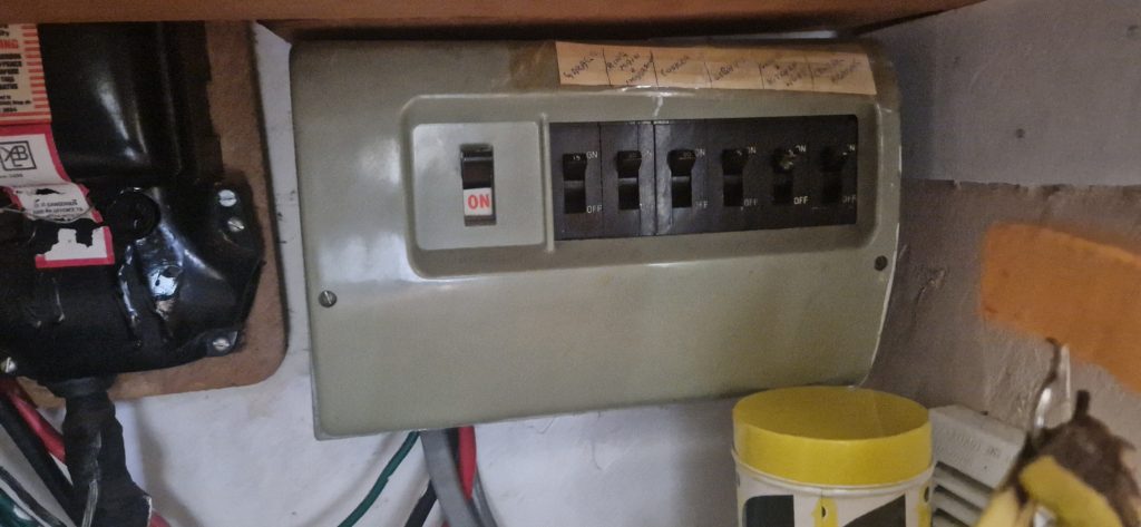 Old plastic fuse board with rewirable fuses and handwritten circuit labels, before replacement with a modern consumer unit
